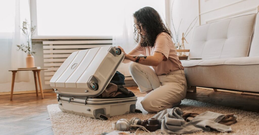 A woman packing her suitcase in a stylish living room, surrounded by clothes and travel accessories.