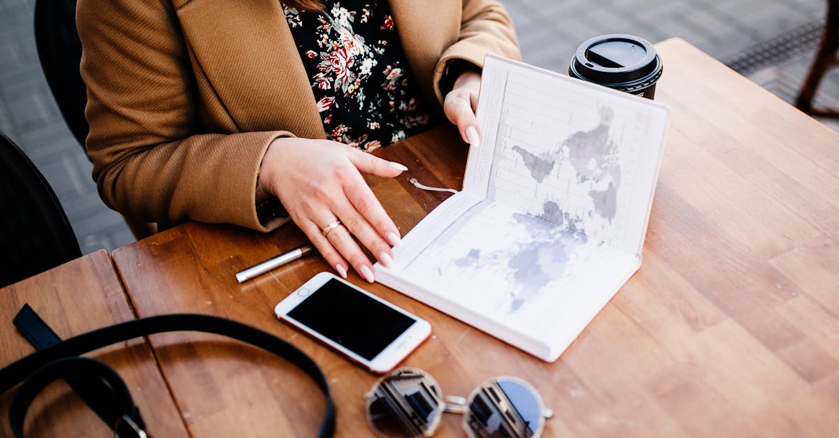 A woman views a travel planner and map on a wooden table, accompanied by coffee and a smartphone.